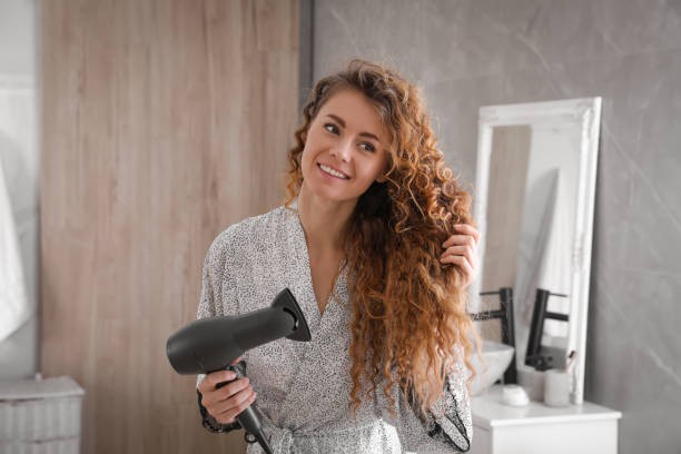 Woman with curly hair scrunching the ends, holding a hairdryer