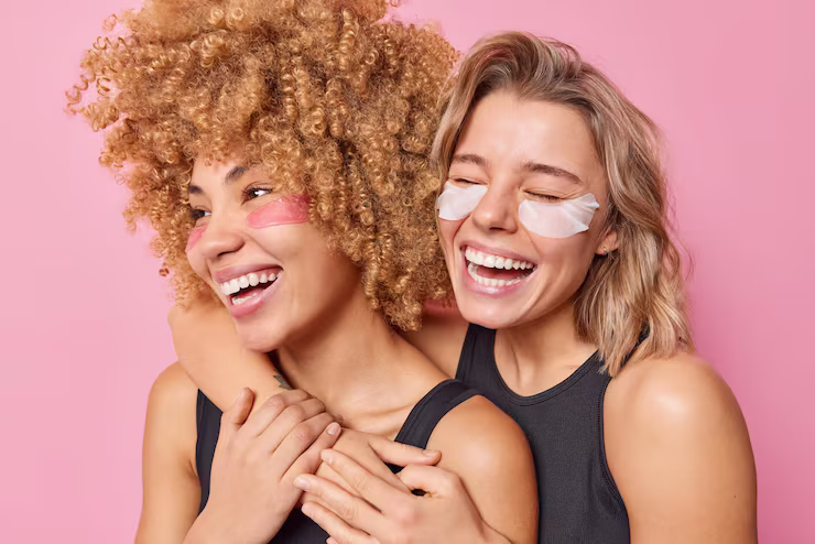 Two friends hugging, whilst wearing under-eye masks and laughing